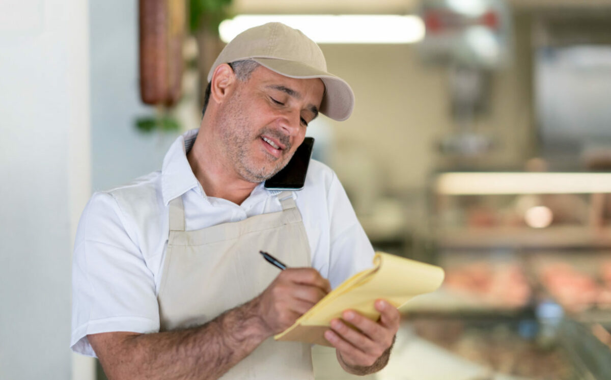 Portrait of a happy man working at a butcher's shop taking a delivery order on the phone and smiling